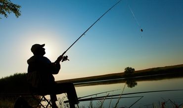 Homem sentado pescando na beira do lago de um pesqueiro.